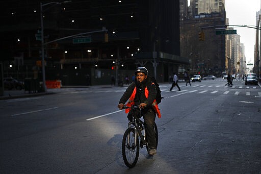 A delivery worker rides up 6th Avenue sparsely populated due to COVID-19 concerns, Friday, March 20, 2020, in New York. New York Gov. Andrew Cuomo is ordering all workers in non-essential businesses to stay home and banning gatherings statewide. &quot;Only essential businesses can have workers commuting to the job or on the job,&quot; Cuomo said of an executive order he will sign Friday. Nonessential gatherings of individuals of any size or for any reason are canceled or postponed. (AP Photo/John Minchillo)