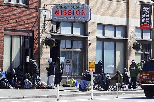 People gather on the sidewalk in front of the Union Gospel Mission in downtown Seattle, Friday, March 20, 2020. The Mission serves a large portion of Seattle's homeless population, and officials fear that controlling the spread of the new coronavirus in groups that lack access to basic hygiene and other supplies will be difficult. (AP Photo/Ted S. Warren)