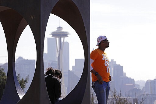 Issa Barry looks out over the Seattle skyline, including the iconic Space Needle, as he stands near a sculpture at a popular park Friday, March 20, 2020. People in the state are being asked to maintain physical distance from others to help stop the spread of COVID-19. The death toll in Washington state from the coronavirus increased to 74 a day earlier, and the number of cases topped 1,300, according to state health officials. (AP Photo/Elaine Thompson)