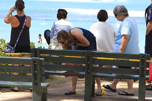 A beachgoer uses a sanitary wipe to clean off a bench before sitting down in Waikiki, Friday, March 20, 2020, in Honolulu. Honolulu closed all public parks and recreation areas Friday until the end of April in an effort to help stop the spread of the coronavirus. (AP Photo/Marco Garcia)