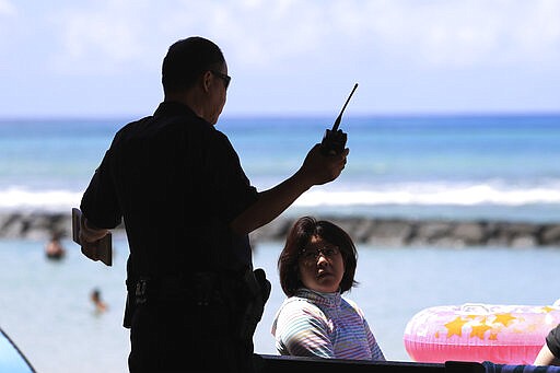 A Honolulu police officer informs beachgoers the park is closed and they must leave the area in Waikiki, Friday, March 20, 2020, in Honolulu. Honolulu closed all public parks and recreation areas Friday until the end of April in an effort to help stop the spread of the coronavirus. While the parks are closed, access to the shoreline was not shut off. (AP Photo/Marco Garcia)