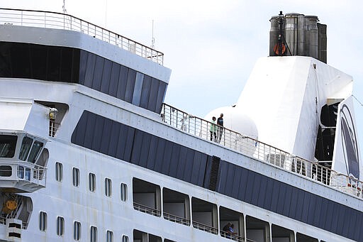 UPDATES THAT SOME PASSENGERS WERE ALLOWED OFF FRIDAY - Two people are seen aboard the Maasdam cruise ship while it is docked in Honolulu Harbor for a re-supply Friday, March 20, 2020, in Honolulu. Six Hawaii residents were allowed to leave the cruise ship and two other U.S. citizens were allowed to disembark for medical reasons  (AP Photo/Marco Garcia)