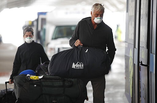 Travelers wear protective masks as they load baggage on a shuttle bus destined for a rental car outlet outside Denver International Airport as people deal with the spread of coronavirus Friday, March 20, 2020, in Denver. According to the World Health Organization, most people recover in about two to six weeks depending on the severity of the COVID-19 illness. (AP Photo/David Zalubowski)