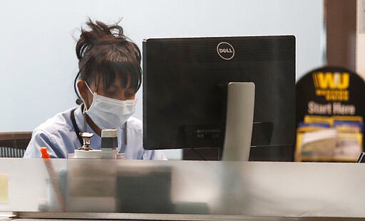 A currency exchange worker wears a mask as she works on a computer in her kiosk in Denver International Airport as travelers and workers deal with the spread of coronavirus Friday, March 20, 2020, in Denver. According to the World Health Organization, most people recover in about two to six weeks depending on the severity of the COVID-19 illness. (AP Photo/David Zalubowski)