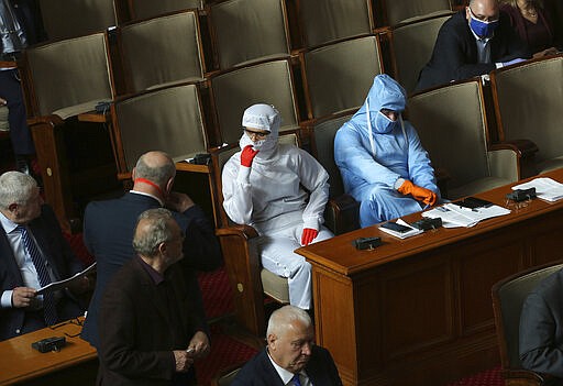 Vesselin Mareshki, right, leader of Bulgarian Political party Volya, and an MP from from his party wear protective suits during Parliamentary session in the Bulgarian National Assembly in Sofia, Bulgaria, on Friday March 20, 2020. For some people the COVID-19 coronavirus causes mild or moderate symptoms, but for some it can cause very severe illness.(AP Photo/Vesselin Borishev)