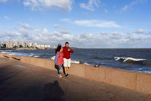 In this March 19, 2020 photo, Marina and Fabio walk arm and arm by the seaside as they drink &quot;mate&quot; in Montevideo, Uruguay. In Uruguay, Paraguay and Argentina, drinking and sharing the herb &quot;mate&quot; is a tradition among family members, office colleagues and schoolmates, who share the straw as they pass the drink around. Today, however, the new coronavirus outbreak has made people quit sharing, to prevent spreading COVID-19. (AP Photo/Matilde Campodonico)