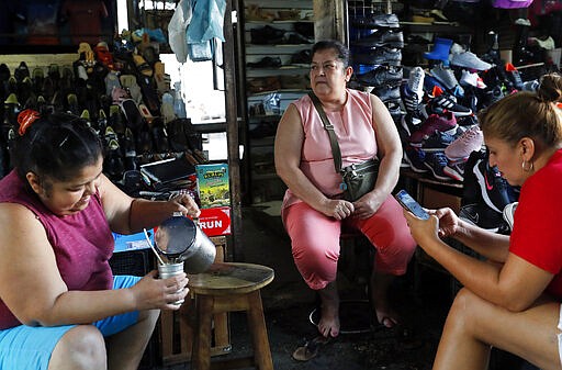 In this March 17, 2020 photo, Otilia Olivera, left, serves cold &quot;mate,&quot; known as &quot;teretere,&quot; for her friends Lidia Silva, center, and Rosa Benitez at Mercado 4 in Asuncion, Paraguay. The friends said they plan to continue drinking mate together, as is social custom.  In Uruguay, Paraguay and Argentina, drinking and sharing the herb &quot;mate&quot; is a tradition among family members, office colleagues and schoolmates, who share the straw as they pass the drink around. Today, however, the new coronavirus outbreak has made some people quit sharing, to prevent spreading COVID-19. (AP Photo/Jorge Saenz)