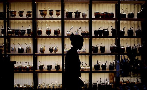 In this March 17, 2020 photo, Paola Garcia walks past herbal &quot;mate&quot; mugs at the shop where she works in Buenos Aires, Argentina, Tuesday, March 17, 2020. In Uruguay, Paraguay and Argentina, drinking and sharing the herbal drink is a custom among family members, office colleagues and schoolmates, who pass the drink around and use the same straw. Today, however, the new coronavirus outbreak has made people quit sharing, to prevent spreading COVID-19. (AP Photo/Natacha Pisarenko)