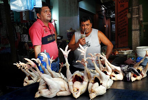 In this March 17, 2020 photo, Anibal Meza, right, and Juan Benitez share cold &quot;mate&quot; at their chicken stall at Mercado 4 in Asuncion, Paraguay. Both men agreed they'd never quit the communal drink but would consider drinking their own individual mugs.  In Uruguay, Paraguay and Argentina, drinking and sharing the herb &quot;mate&quot; is a tradition among family members, office colleagues and schoolmates, who share the straw as they pass the drink around. Today, however, the new coronavirus outbreak has made people quit sharing, to prevent spreading COVID-19.  (AP Photo/Jorge Saenz)