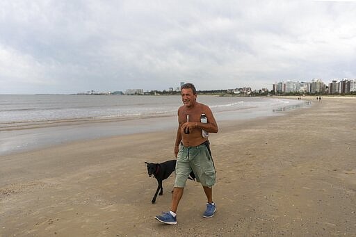 In this  March 17, 2020 photo, Omar walks on the beach clutching his thermos and &quot;mate,&quot; in Montevideo, Uruguay.  In Uruguay, Paraguay and Argentina, drinking and sharing the herb &quot;mate&quot; is a tradition among family members, office colleagues and schoolmates, who share the straw as they pass the drink around. Today, however, the new coronavirus outbreak has made people quit sharing, to prevent spreading COVID-19. (AP Photo/Matilde Campodonico)