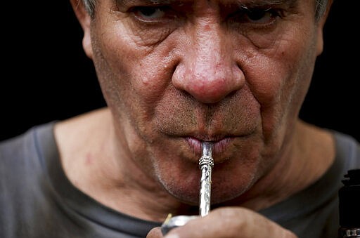 In this March 17, 2020 photo, Oscar Brun drinks &quot;mate&quot; at his ironworks shop in Buenos Aires, Argentina. Brun said one prepares &quot;mate&quot; to share it and be social. In Uruguay, Paraguay and Argentina, drinking and sharing the herb &quot;mate&quot; is a tradition among family members, office colleagues and schoolmates, who share the straw as they pass the drink around. Today, however, the spread of the new coronavirus outbreak has made people quit sharing. (AP Photo/Natacha Pisarenko)