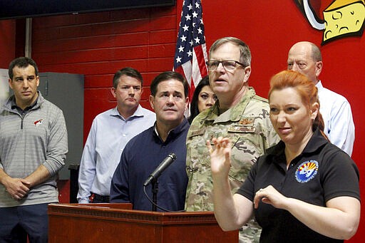 Gov. Doug Ducey, left in blue jacket, looks on as Arizona National Guard commander Maj. Gen. Michael McGuire briefs reporters on the Guard's response to the coronavirus crisis at St. Mary's Food Bank in Phoenix Friday, March 20, 2020 . Ducey ordered the Guard to help grocers restock their shelves after they were depleted by panic buying, and urged people to volunteer and donate to depleted food banks. (AP Photo/Bob Christie)