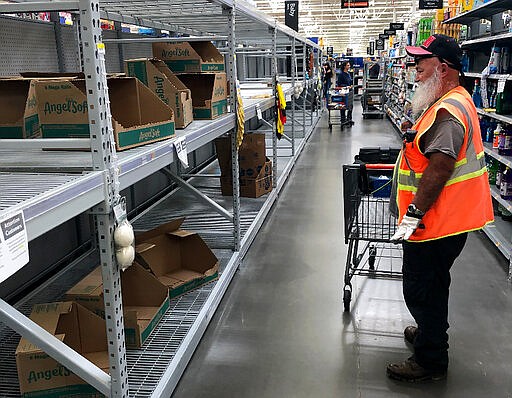 A shopper looks at a cleaned-out toilet paper aisle in a Phoenix Walmart Supercenter Friday, March 20, 2020. Arizona Gov. Doug Ducey said he's activating the National Guard to help grocery stores and food banks, halting elective surgeries and closing businesses in areas with known cases of COVID-19. (AP Photo/Bob Christie)