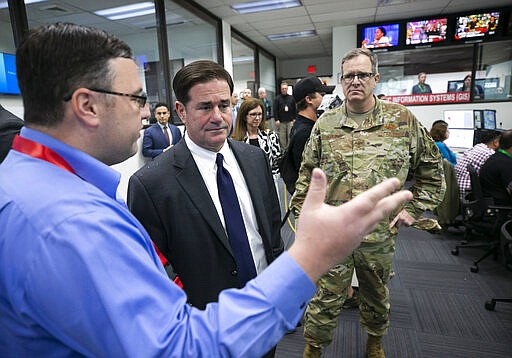 Arizona governor Doug Ducey, center, talks to Matt Heckard, left, assistant director of preparedness, with the State of Arizona Department of Emergency and Military Affairs (DEMA) as members of DEMA work responding to the coronavirus pandemic, in the DEMA operations center at the Arizona National Guard Papago Park Military Reservation in Phoenix on Wednesday, March 18, 2020. Major General Michael T. McGuire (background right) the director of DEMA, looks on. (David Wallace/The Arizona Republic via AP, Pool)