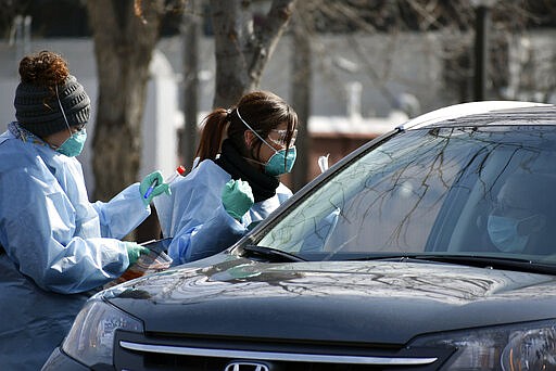 Emergency department technician Katrina Malson, left, and critical care nurse Molly Spaeny, center, test a patient for coronavirus in a drive-thru testing center outside the hospital in Billings, Mont. Friday, March 20, 2020. For most people, the new coronavirus causes only mild or moderate symptoms, such as fever and cough. For some, especially older adults and people with existing health problems, it can cause more severe illness, including pneumonia.(AP Photo/Matthew Brown)