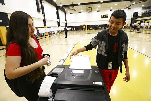 In this March 5, 2020, photo Nicole Pardo, left, plays the part of an election official as she checks students ingesting their ballots as they participate in their own Democratic presidential preference election and voter registration drive at Maryvale High School in Phoenix. At the school hundreds of students who will turn 18 before Election Day were registered to vote. (AP Photo/Ross D. Franklin)