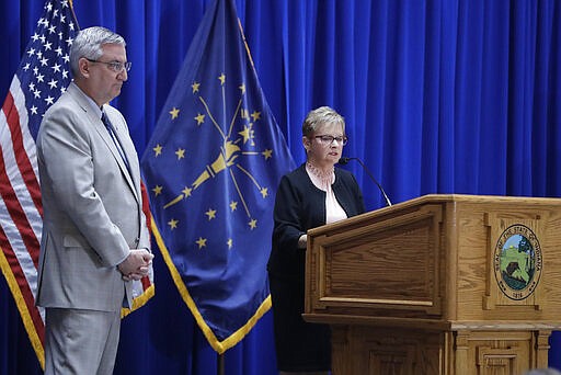 Indiana Gov. Eric Holcomb listens as Secretary of State Connie Lawson speaks during a news conference at the Statehouse, Friday, March 20, 2020, in Indianapolis. Holcomb said during the news conference with the state GOP and Democratic chairmen that the Indiana primary will be held on June 2 because of concern about the coronavirus pandemic. (AP Photo/Darron Cummings)