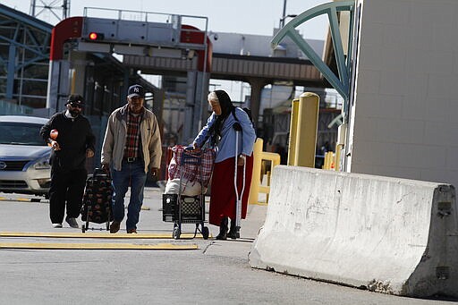 Silvia Shadden, 68, in blue, pulls a cart as she leaves a U.S. customs checkpoint in El Paso, Texas after a she went to Ciudad Juarez, Mexico for a doctor's appointment on Friday, March 20, 2020. Shadden, of El Paso, says she needs a weekly vitamin injection to prevent muscle atrophy. Her medicine costs $10 in Ciudad Juarez and $70 in El Paso. She walks more than a mile to get the treatment. She fears that the border may close and she won't be able to afford medicine in the U.S. (AP Photo/Cedar Attanasio)