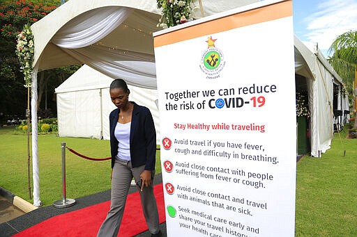 A woman walks past a coronavirus awareness campaign poster at State House in Harare, Thursday, March, 19, 2020. For most people, the new coronavirus causes only mild or moderate symptoms. For some it can cause more severe illness, especially in older adults and people with existing health problems. (AP Photo/Tsvangirayi Mukwazhi)
