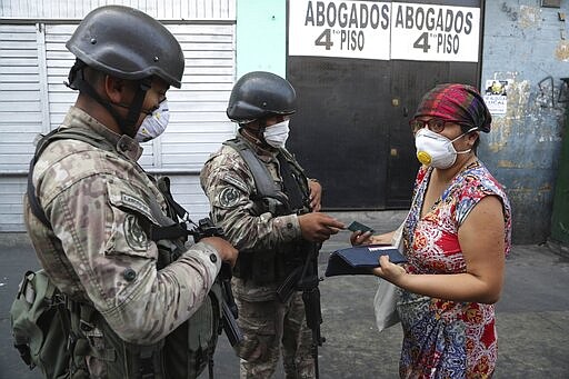 A woman explains to soldiers that she is searching pharmacies for alcohol, before they let her continue on her way, on the third day of a state of emergency in Lima, Peru, Wednesday, March 18, 2020. Peru's President Martin Vizcarra ordered residents to stay in their homes and temporarily suspended certain constitutional rights in an effort to contain the spread of the new coronavirus. The vast majority of people recover from the new virus. (AP Photo/Martin Mejia)