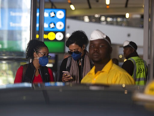 In this photograph taken Thursday March 19, 2020, travelers wear masks as they walks through O.R. Tambo airport in Johannesburg, South Africa.  Some countries around the world lack the equipment and trained health workers to respond to the threat of COVID-19 virus. For most people the virus causes mild or moderate symptoms, but for others it causes severe illness.  (AP Photo/Denis Farrell)