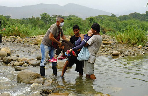 A Venezuelan woman is help by men as he crosses illegally into Colombia from Venezuela, near the Simon Bolivar International Bridge in La Parada near Cucuta, Colombia, Saturday, March 14, 2020. Colombian President Ivan Duque has ordered the nation's border with Venezuela closed as a coronavirus containment measure. (AP Photo/Antonio Ospina)