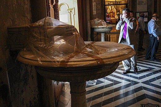 Plastic covers a communal holy water font, used by people who dip their fingers into the water then make a sign of the cross on their foreheads, as a precaution against the spread of the new coronavirus at the Cathedral in Santiago, Chile, Wednesday, March 18, 2020. The vast majority of people recover from COVID-19. (AP Photo/Esteban Felix)