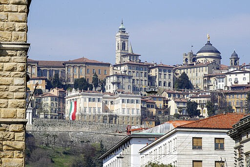 FILE - In this Tuesday, March 17, 2020 filer, a large flag of Italy hangs from the facade of Palazzo Medolago Albani in Bergamo Alta, the top part of the city, in Bergamo, the heart of the hardest-hit province in Italy&#146;s hardest-hit region of Lombardy, Italy, Tuesday, March 17, 2020. For most people, the new coronavirus causes only mild or moderate symptoms. For some it can cause more severe illness, especially in older adults and people with existing health problems. (AP Photo/Luca Bruno, File)