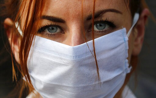 An member of the group 'Pause the System' wears a face mask as she protests in front of the entrance to Downing Street in London, Friday, March 20, 2020. For most people, the new coronavirus causes only mild or moderate symptoms, such as fever and cough. For some, especially older adults and people with existing health problems, it can cause more severe illness, including pneumonia. (AP Photo/Frank Augstein)