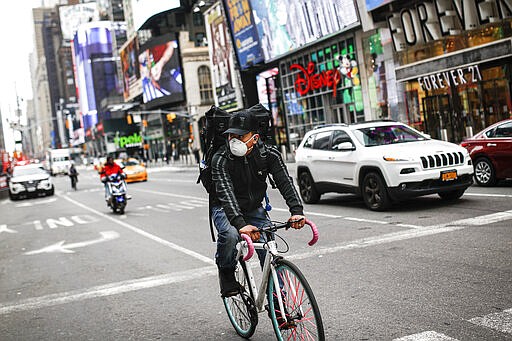 A bicycle delivery worker wears a protective face mask as he rides through a sparsely populated Times Square due to COVID-19 concerns, Friday, March 20, 2020, in New York. New York Gov. Andrew Cuomo is ordering all workers in non-essential businesses to stay home and banning gatherings statewide. &quot;Only essential businesses can have workers commuting to the job or on the job,&quot; Cuomo said of an executive order he will sign Friday. Nonessential gatherings of individuals of any size or for any reason are canceled or postponed. (AP Photo/John Minchillo)