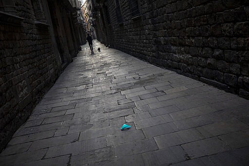 A face mask on the ground as a woman walks with her dog along a street in downtown Barcelona, Spain, Friday, March 20, 2020. For most people, the new coronavirus causes only mild or moderate symptoms. For some, it can cause more severe illness, especially in older adults and people with existing health problems. (AP Photo/Emilio Morenatti)