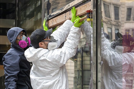 Carpenters wear protective gear as they board up the closed Sephora store on 34th St., Friday, March 20, 2020, in New York. New York Gov. Andrew Cuomo is ordering all workers in non-essential businesses to stay home and banning gatherings statewide. &quot;Only essential businesses can have workers commuting to the job or on the job,&quot; Cuomo said of an executive order he will sign Friday. Nonessential gatherings of individuals of any size or for any reason are canceled or postponed. (AP Photo/Mary Altaffer)