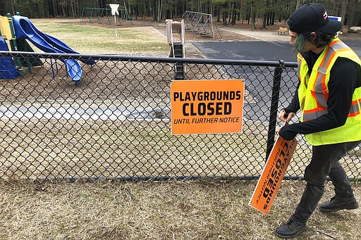 A Department of Public Works worker places a closed sign near an entrance to a playground at an elementary school, in Walpole, Mass., Friday, March 20, 2020, out of concern about the spread of the coronavirus. For most people, the new coronavirus causes only mild or moderate symptoms, such as fever and cough. For some, especially older adults and people with existing health problems, it can cause more severe illness, including pneumonia. The vast majority of people recover from the new virus. (AP Photo/Steven Senne)