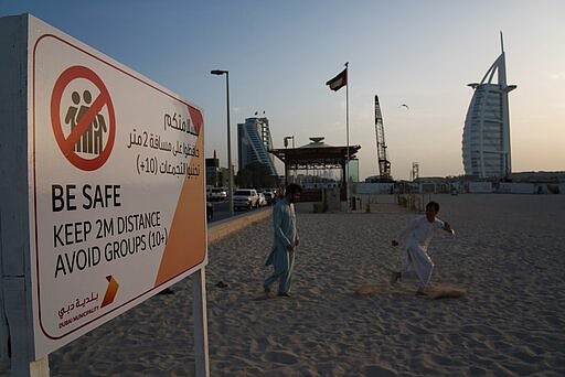 Two laborers play tag near a sign warning people to maintain a distance from each other over the outbreak of the new coronavirus in front of the sail-shaped Burj Al Arab luxury hotel in Dubai, United Arab Emirates, Friday, March 20, 2020. The United Arab Emirates has closed its borders to foreigners, including those with residency visas, over the coronavirus outbreak, but has yet to shut down public beaches and other locations over the virus. (AP Photo/Jon Gambrell)