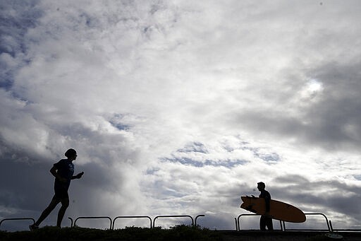 A surfer and jogger make their way along the bike path in the dog beach area of Huntington Breach, Calif. on Thursday, March 19, 2020. (AP Photo/Chris Carlson)