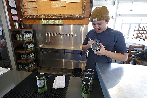 Max Navarro, assistant manager of Fieldwork Brewing Co. marks 32 ounce crowlers for online pickup at the Oxbow Public Market Thursday, March 19, 2020, in Napa, Calif. The brewery's taproom is closed, but customers can order online for pickup or curbside delivery. As worries about the spread of the coronavirus confine millions of Californians to their homes, concern is growing about those who have no homes in which to shelter. (AP Photo/Eric Risberg)