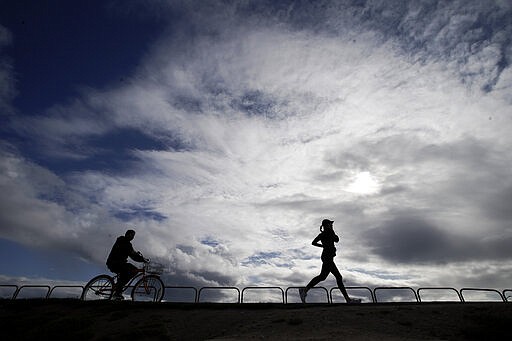 A bicyclist and jogger make their way along the bike path in the dog beach area of Huntington Breach, Calif. on Thursday, March 19, 2020. (AP Photo/Chris Carlson)