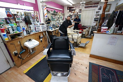 Carlos Vasquez, left, and his nephew R.J. Vasquez, wait for customers at their family's barber shop Friday, March 20, 2020, in Houston. The barbers at family-owned barber shop estimate they have lost nearly half of their business due to the coronavirus. (AP Photo/David J. Phillip)