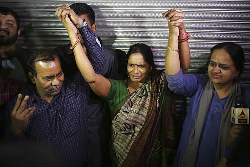 Badrinath, left, Asha Devi, center, parents of the victim of the fatal 2012 gang rape on a moving bus, hold hands as they react after the rapists of her daughter were hanged, in New Delhi, India, Friday, March 20, 2020. Four men were sentenced to capital punishment for the 2012 gang-rape of a 23-year-old physiotherapy student on a moving bus in New Delhi have been executed. (AP Photo/Altaf Qadri)