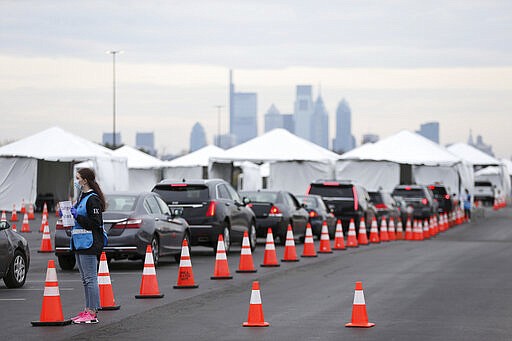 Philadelphia Medical Reserve Corps volunteer Emma Ewing, left, a sophomore at Temple University, directs cars at the city's coronavirus testing site next to Citizens Bank Park in South Philadelphia on Friday, March 20, 2020. The site, which opened Friday afternoon, is the first city-run drive-through location where people can be swabbed to determine if they have the coronavirus. At the time of opening, it was only for people with symptoms who are over 50 and healthcare workers with symptoms. (Tim Tai/The Philadelphia Inquirer via AP)