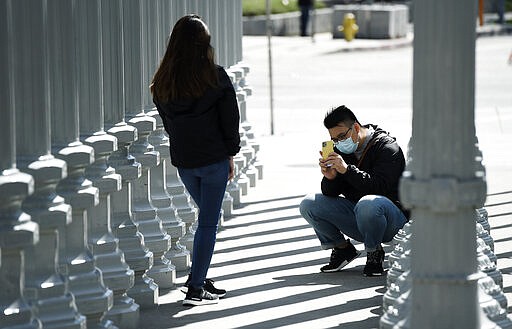 Visitors to artist Chris Burden's &quot;Urban Light&quot; art installation outside the Los Angeles County Museum of Art take pictures of each other, Wednesday, March 18, 2020, in Los Angeles. (AP Photo/Chris Pizzello)