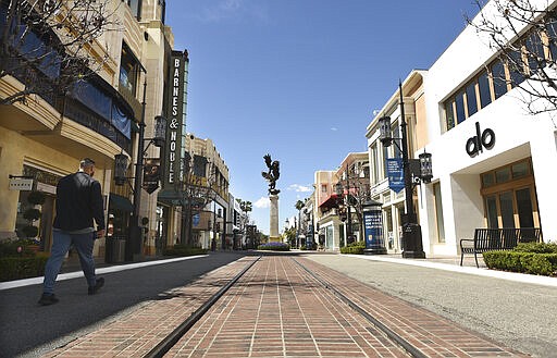 A visitor to the shopping and entertainment complex The Grove walks down a deserted street Wednesday, March 18, 2020, in Los Angeles. (AP Photo/Chris Pizzello)