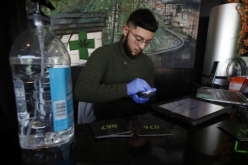 The Green Cross cannabis dispensary employee Sam, who did not want to give his last name, uses a disinfecting cleaning wipe on numbered cards that are handed to customers in San Francisco, Wednesday, March 18, 2020. As about 7 million people in the San Francisco Bay Area are under shelter-in-place orders, only allowed to leave their homes for crucial needs in an attempt to slow virus spread, marijuana stores remain open and are being considered &quot;essential services.&quot; (AP Photo/Jeff Chiu)