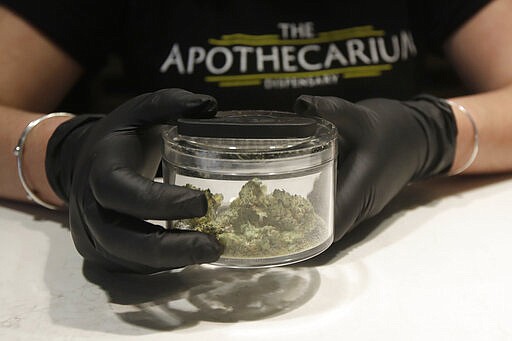 Cali Manzello, general manager at The Apothecarium cannabis dispensary, wears gloves when holding a marijuana sample for smelling while posing for photos at the store in San Francisco, Wednesday, March 18, 2020. As about 7 million people in the San Francisco Bay Area are under shelter-in-place orders, only allowed to leave their homes for crucial needs in an attempt to slow virus spread, marijuana stores remain open and are being considered &quot;essential services.&quot; (AP Photo/Jeff Chiu)