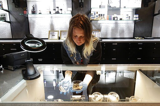 Budtender Varv Pavlova wears gloves while posing for photos handling marijuana samples under a magnifying glass at The Mission Cannabis Club dispensary in San Francisco, Thursday, March 19, 2020. (AP Photo/Jeff Chiu)