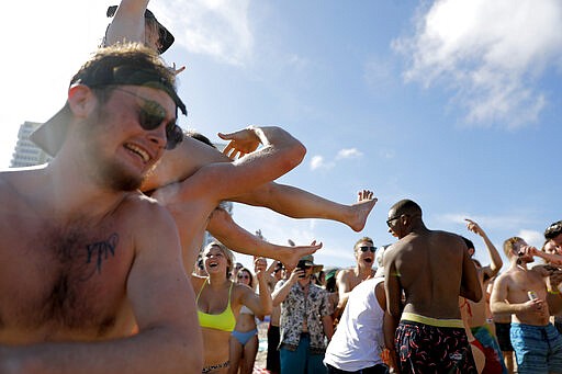 Spring break revelers party on the beach, Tuesday, March 17, 2020, in Pompano Beach, Fla. As a response to the coronavirus pandemic, Florida Gov. Ron DeSantis ordered all bars be shut down for 30 days beginning at 5 p.m. and many Florida beaches are turning away spring break crowds urging them to engage in social distancing. (AP Photo/Julio Cortez)