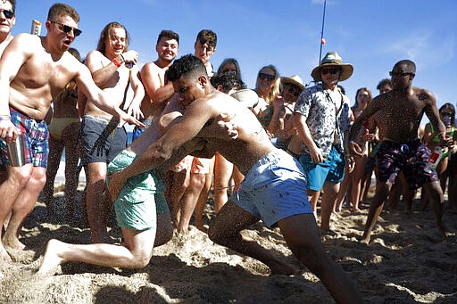 Two men wrestle each other as spring break revelers look on during a contest on the beach, Tuesday, March 17, 2020, in Pompano Beach, Fla. As a response to the coronavirus pandemic, Florida Gov. Ron DeSantis ordered all bars be shut down for 30 days beginning at 5 p.m. and many Florida beaches are turning away spring break crowds urging them to engage in social distancing. (AP Photo/Julio Cortez)