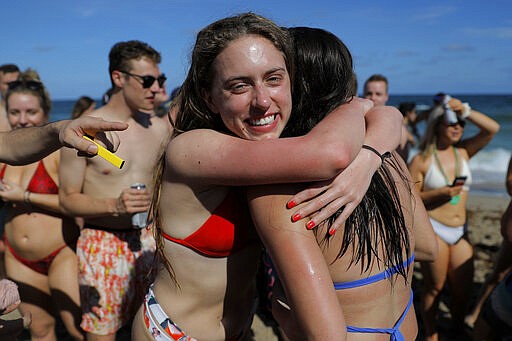 Two spring break revelers hug while partyng in a large crowd on the beach, Tuesday, March 17, 2020, in Pompano Beach, Fla. As a response to the coronavirus pandemic, Florida Gov. Ron DeSantis ordered all bars be shut down for 30 days beginning at 5 p.m. and many Florida beaches are turning away spring break crowds urging them to engage in social distancing. (AP Photo/Julio Cortez)