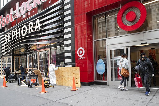 FILE - In this Friday, March 20, 2020 file photo, a shopper leaves the Target Store on 34th St. with supplies as carpenter board up the Sephora story in New York.  Target Corp. said Friday it will give a $2 an hour wage increase to its 300,000-plus workers who have been scrambling to help customers. The pay bump will be effective at least through May 2. (AP Photo/Mary Altaffer, File)