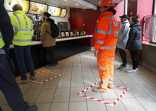 People stand in marked places to keep a social distance at a fast food restaurant in London, Friday, March 20, 2020. For most people, the new coronavirus causes only mild or moderate symptoms, such as fever and cough. For some, especially older adults and people with existing health problems, it can cause more severe illness, including pneumonia. (AP Photo/Frank Augstein)